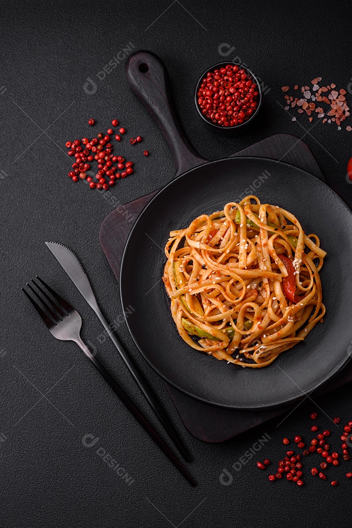 Delicioso prato de udon asiático com legumes, cogumelos, sal e especiarias numa placa cerâmica sobre um fundo escuro de concreto