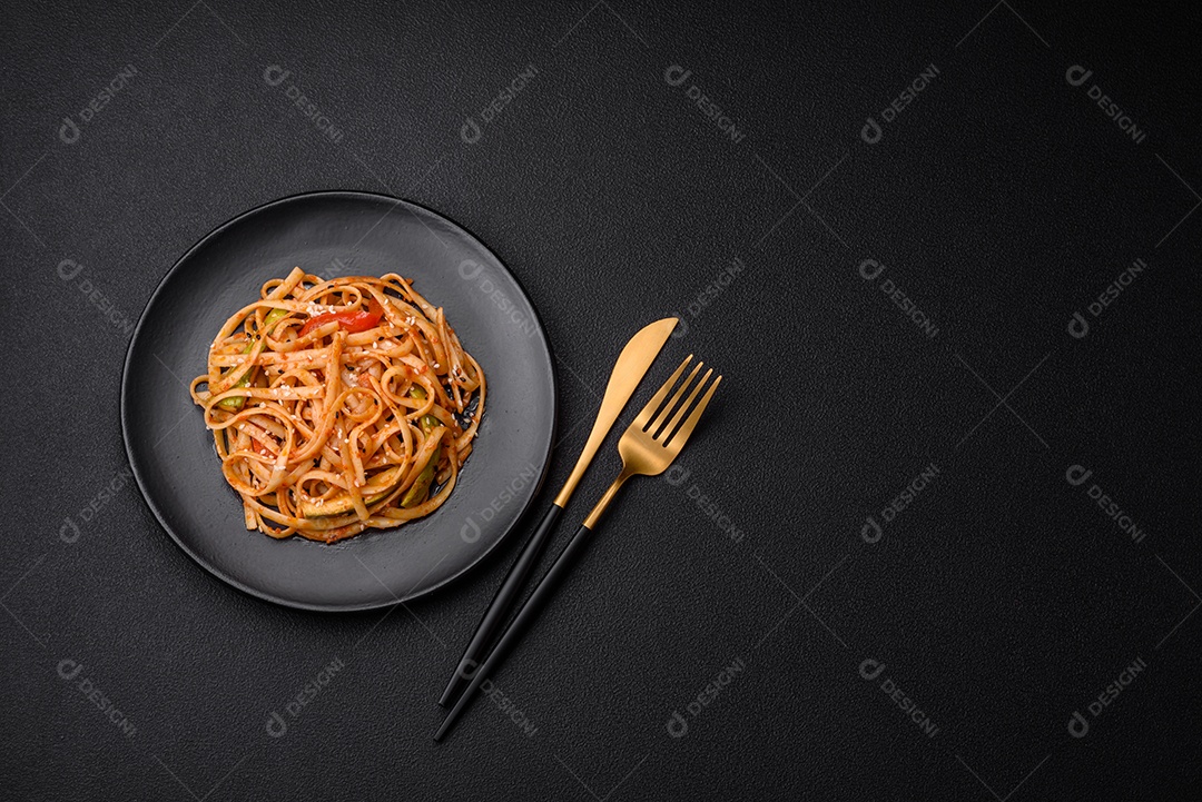 Delicioso prato de udon asiático com legumes, cogumelos, sal e especiarias numa placa cerâmica sobre um fundo escuro de concreto