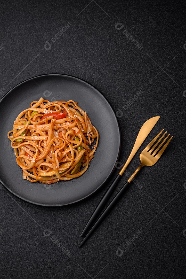 Delicioso prato de udon asiático com legumes, cogumelos, sal e especiarias numa placa cerâmica sobre um fundo escuro de concreto