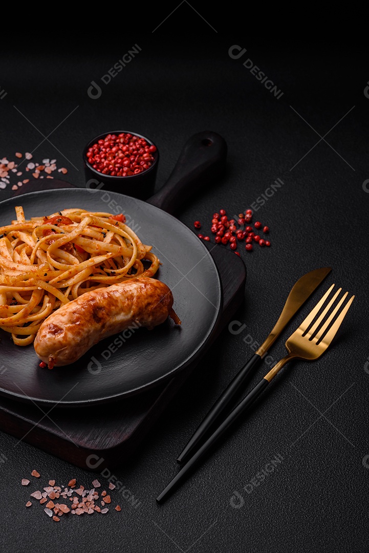 Deliciosa salsicha grelhada suculenta com macarrão ou macarrão com sal, especiarias e ervas em uma placa cerâmica sobre um fundo escuro de concreto