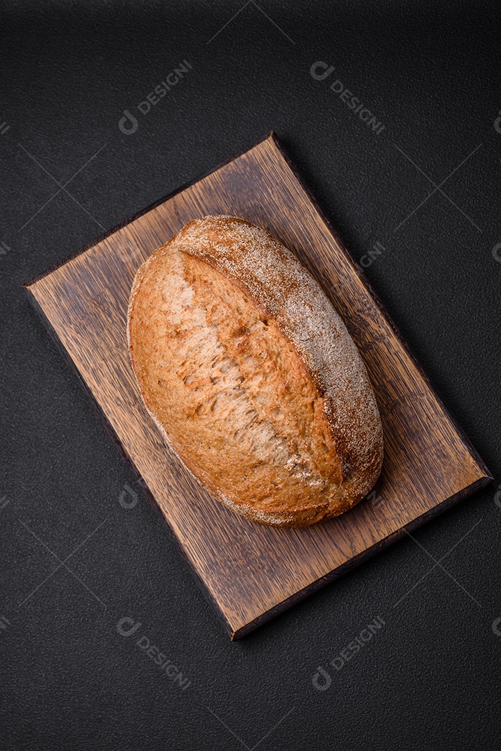 Delicioso pão crocante fresco assado com sementes e grãos sobre um fundo escuro de concreto