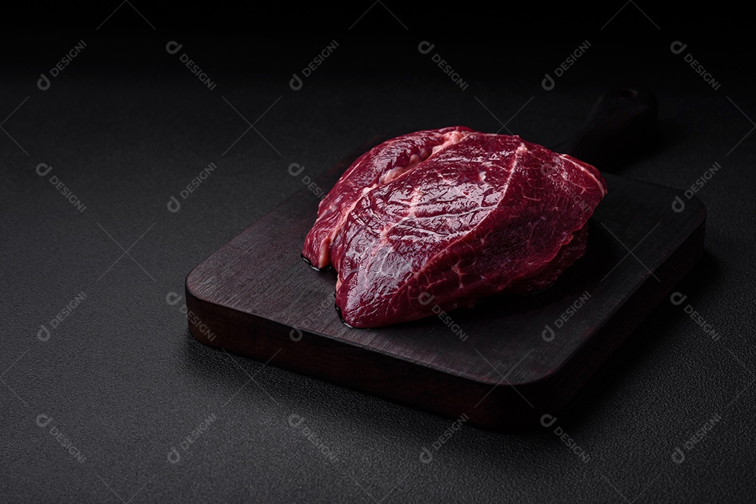 Carne crua suculenta com especiarias, sal e ervas sobre um fundo escuro de concreto. Preparando-se para cozinhar um prato de carne