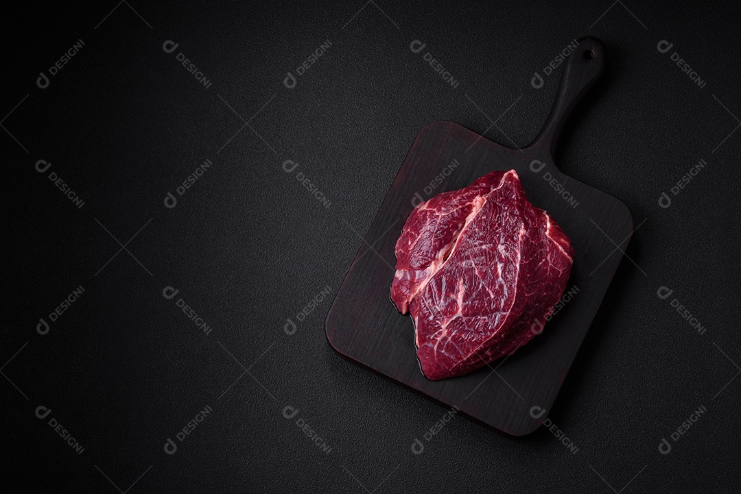 Carne crua suculenta com especiarias, sal e ervas sobre um fundo escuro de concreto. Preparando-se para cozinhar um prato de carne