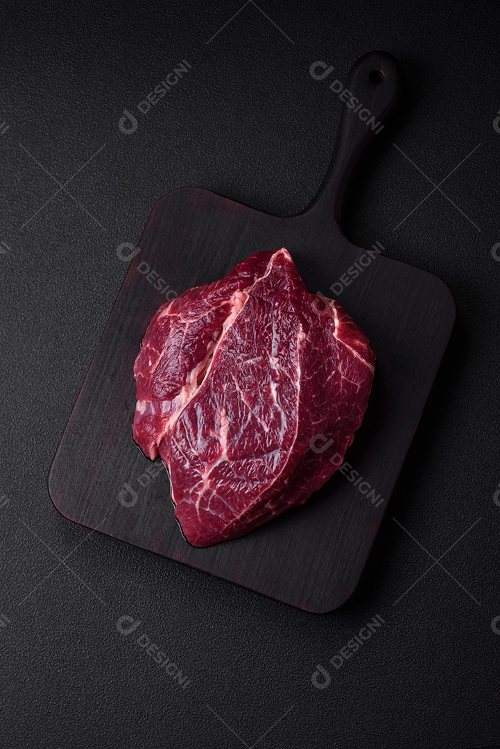 Carne crua suculenta com especiarias, sal e ervas sobre um fundo escuro de concreto. Preparando-se para cozinhar um prato de carne