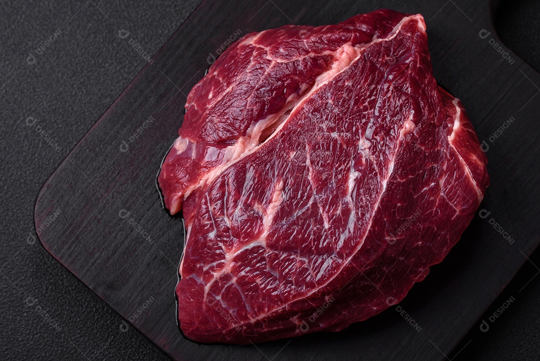 Carne crua suculenta com especiarias, sal e ervas sobre um fundo escuro de concreto. Preparando-se para cozinhar um prato de carne