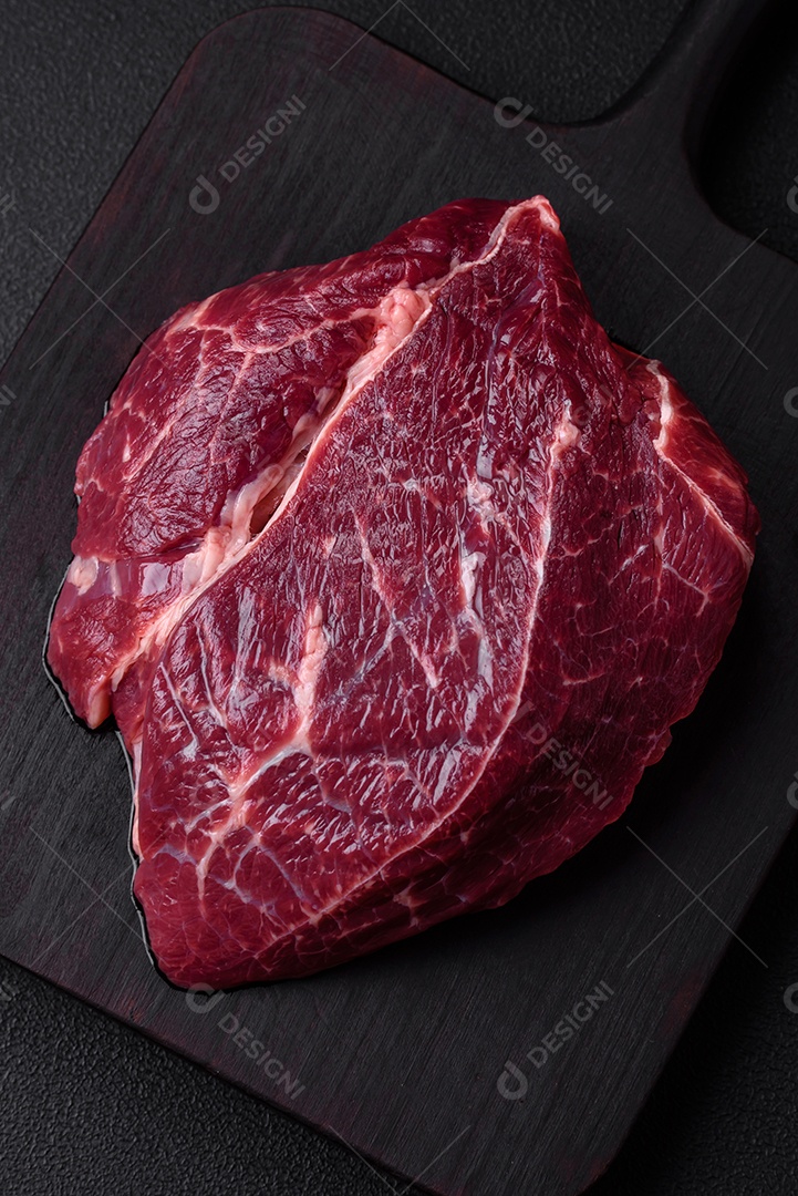 Carne crua suculenta com especiarias, sal e ervas sobre um fundo escuro de concreto. Preparando-se para cozinhar um prato de carne