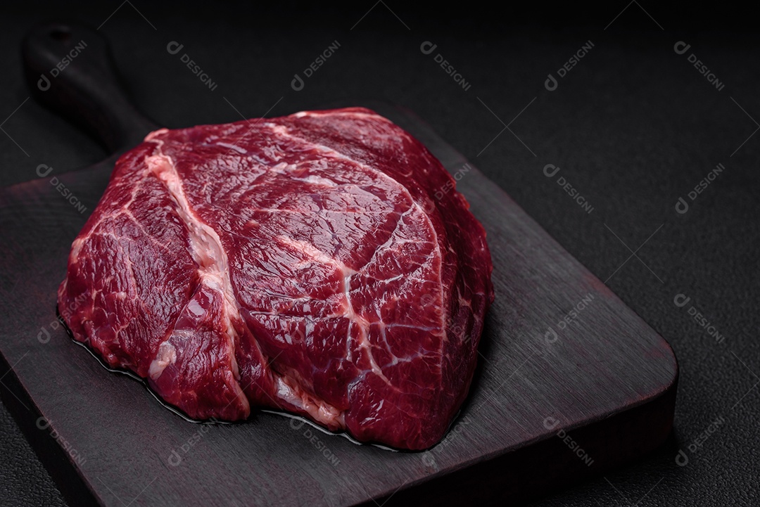 Carne crua suculenta com especiarias, sal e ervas sobre um fundo escuro de concreto. Preparando-se para cozinhar um prato de carne