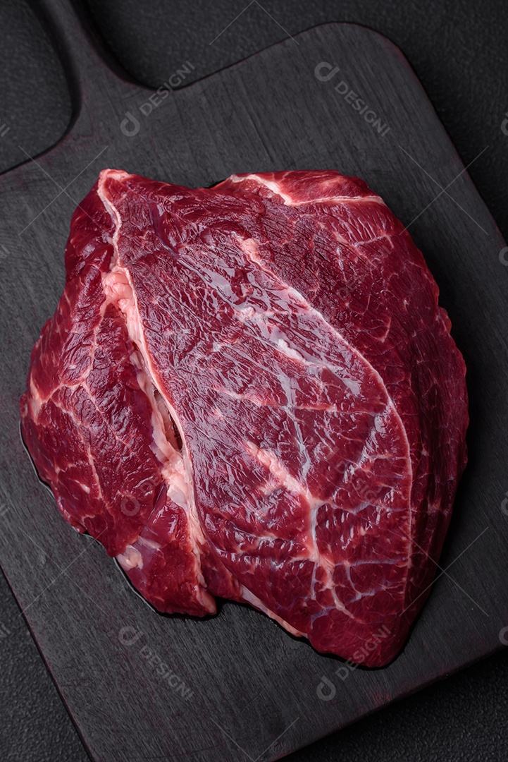 Carne crua suculenta com especiarias, sal e ervas sobre um fundo escuro de concreto. Preparando-se para cozinhar um prato de carne