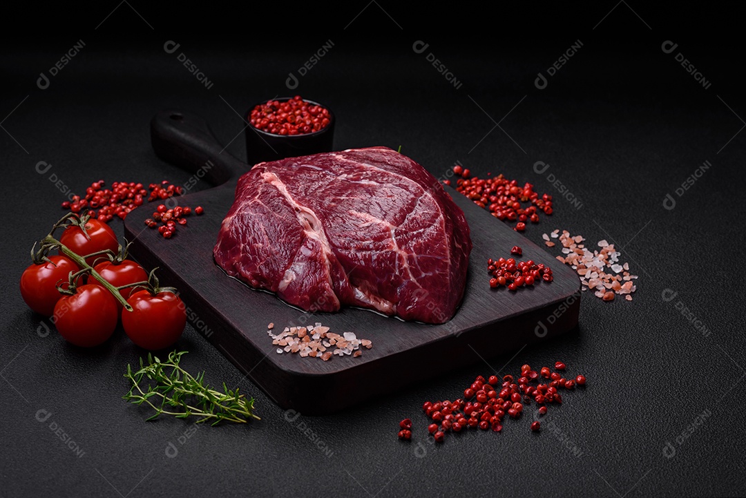 Carne crua suculenta com especiarias, sal e ervas sobre um fundo escuro de concreto. Preparando-se para cozinhar um prato de carne