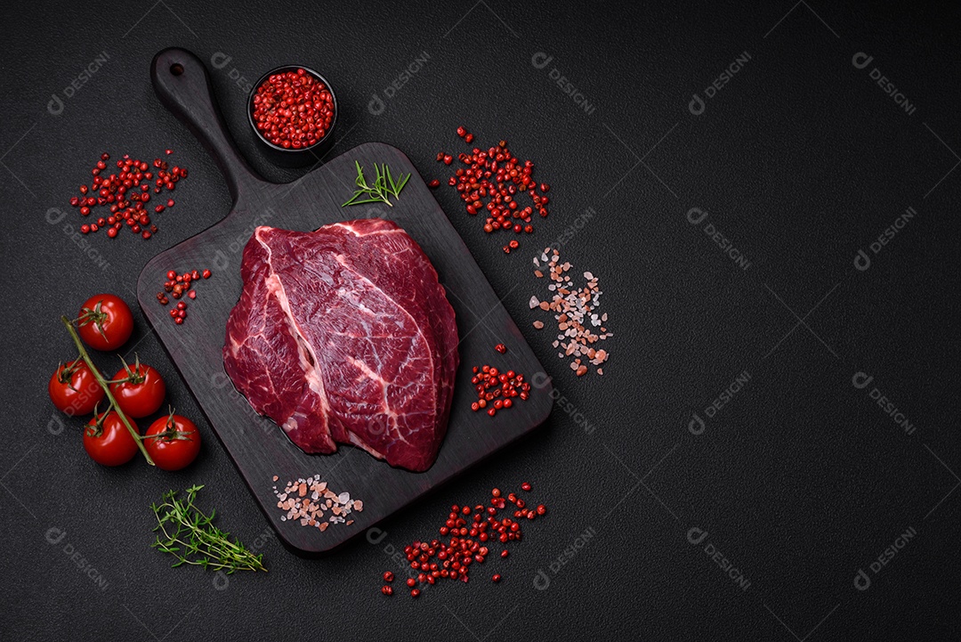 Carne crua suculenta com especiarias, sal e ervas sobre um fundo escuro de concreto. Preparando-se para cozinhar um prato de carne