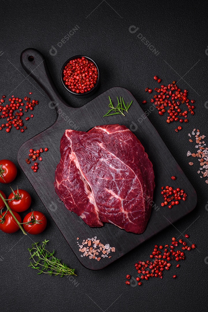 Carne crua suculenta com especiarias, sal e ervas sobre um fundo escuro de concreto. Preparando-se para cozinhar um prato de carne