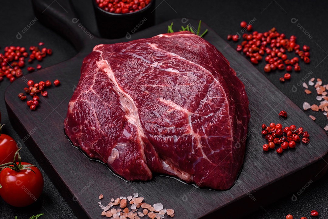 Carne crua suculenta com especiarias, sal e ervas sobre um fundo escuro de concreto. Preparando-se para cozinhar um prato de carne