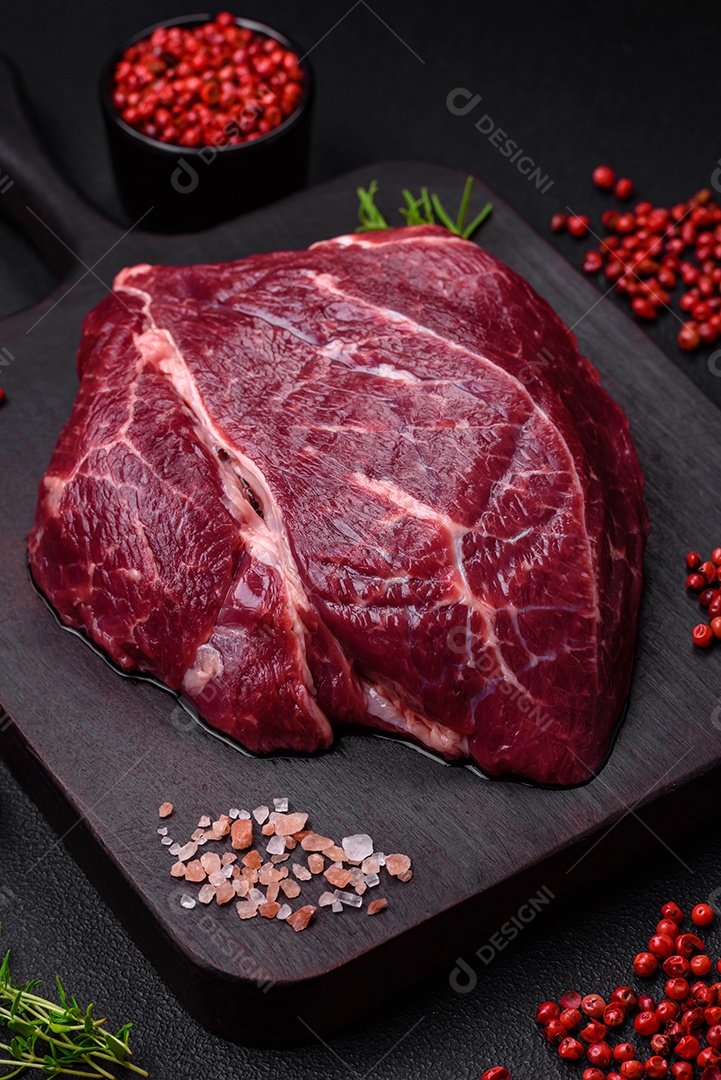 Carne crua suculenta com especiarias, sal e ervas sobre um fundo escuro de concreto. Preparando-se para cozinhar um prato de carne