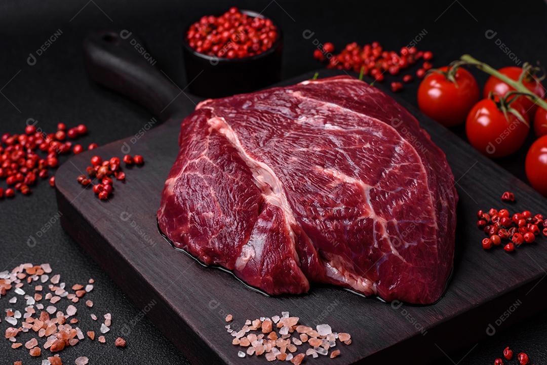 Carne crua suculenta com especiarias, sal e ervas sobre um fundo escuro de concreto. Preparando-se para cozinhar um prato de carne