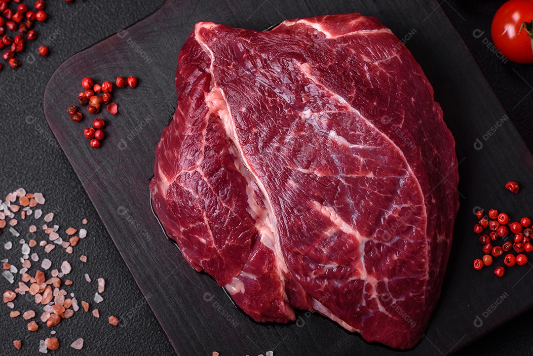 Carne crua suculenta com especiarias, sal e ervas sobre um fundo escuro de concreto. Preparando-se para cozinhar um prato de carne