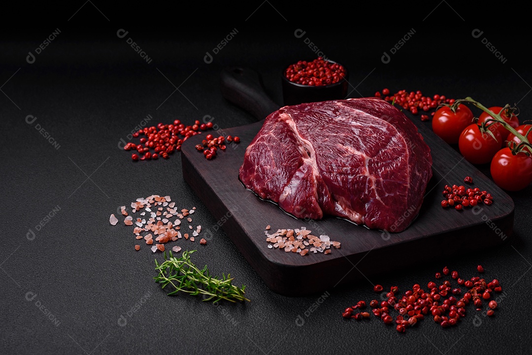 Carne crua suculenta com especiarias, sal e ervas sobre um fundo escuro de concreto. Preparando-se para cozinhar um prato de carne