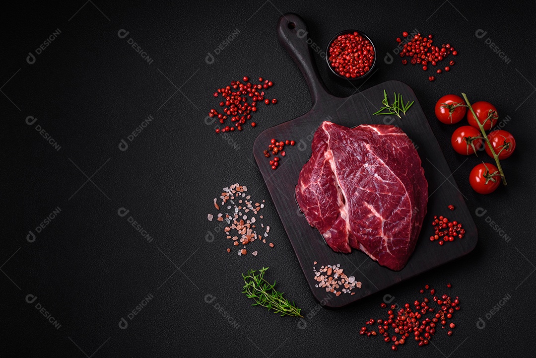 Carne crua suculenta com especiarias, sal e ervas sobre um fundo escuro de concreto. Preparando-se para cozinhar um prato de carne