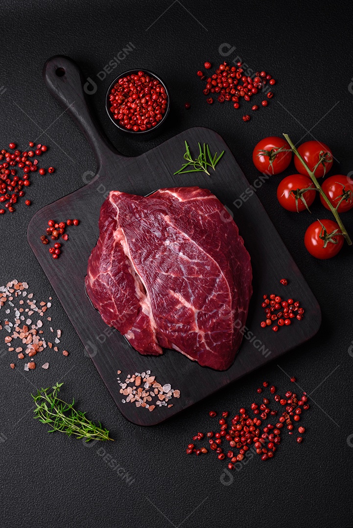 Carne crua suculenta com especiarias, sal e ervas sobre um fundo escuro de concreto. Preparando-se para cozinhar um prato de carne