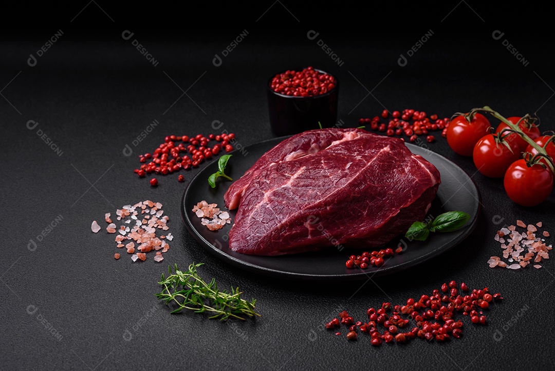 Carne crua suculenta com especiarias, sal e ervas sobre um fundo escuro de concreto. Preparando-se para cozinhar um prato de carne