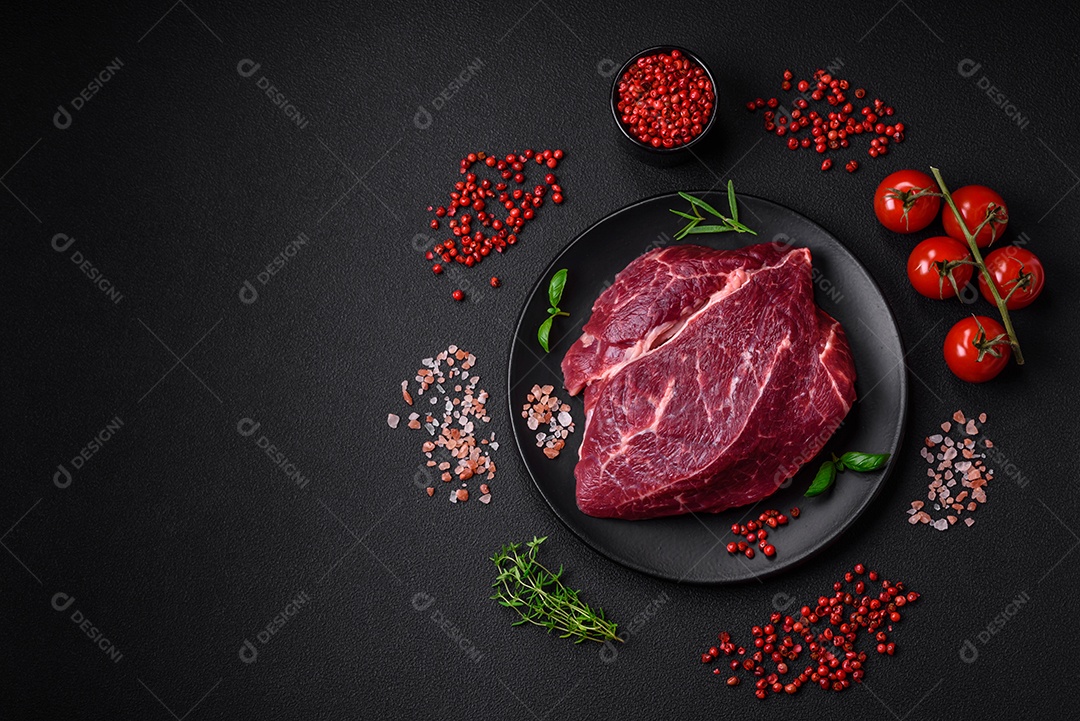 Carne crua suculenta com especiarias, sal e ervas sobre um fundo escuro de concreto. Preparando-se para cozinhar um prato de carne