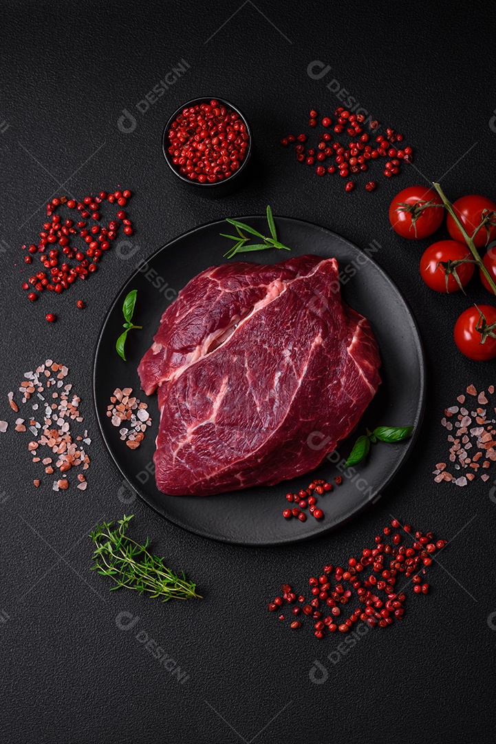Carne crua suculenta com especiarias, sal e ervas sobre um fundo escuro de concreto. Preparando-se para cozinhar um prato de carne