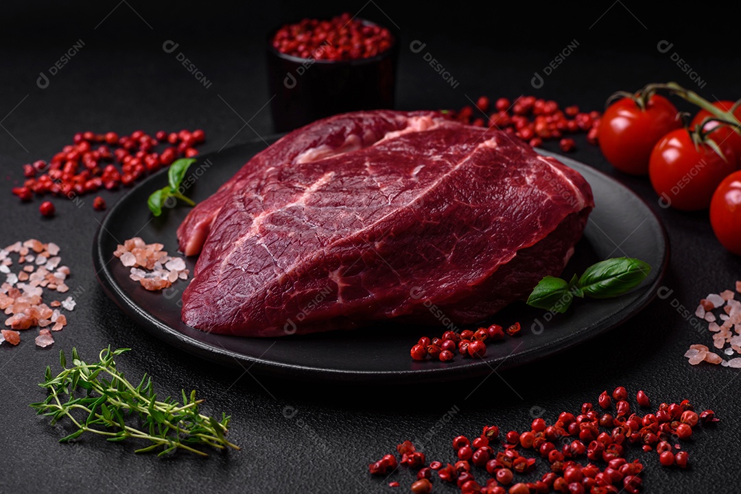 Carne crua suculenta com especiarias, sal e ervas sobre um fundo escuro de concreto. Preparando-se para cozinhar um prato de carne