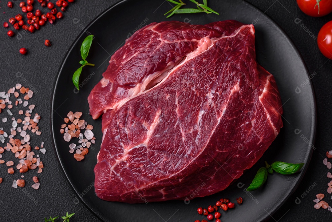 Carne crua suculenta com especiarias, sal e ervas sobre um fundo escuro de concreto. Preparando-se para cozinhar um prato de carne