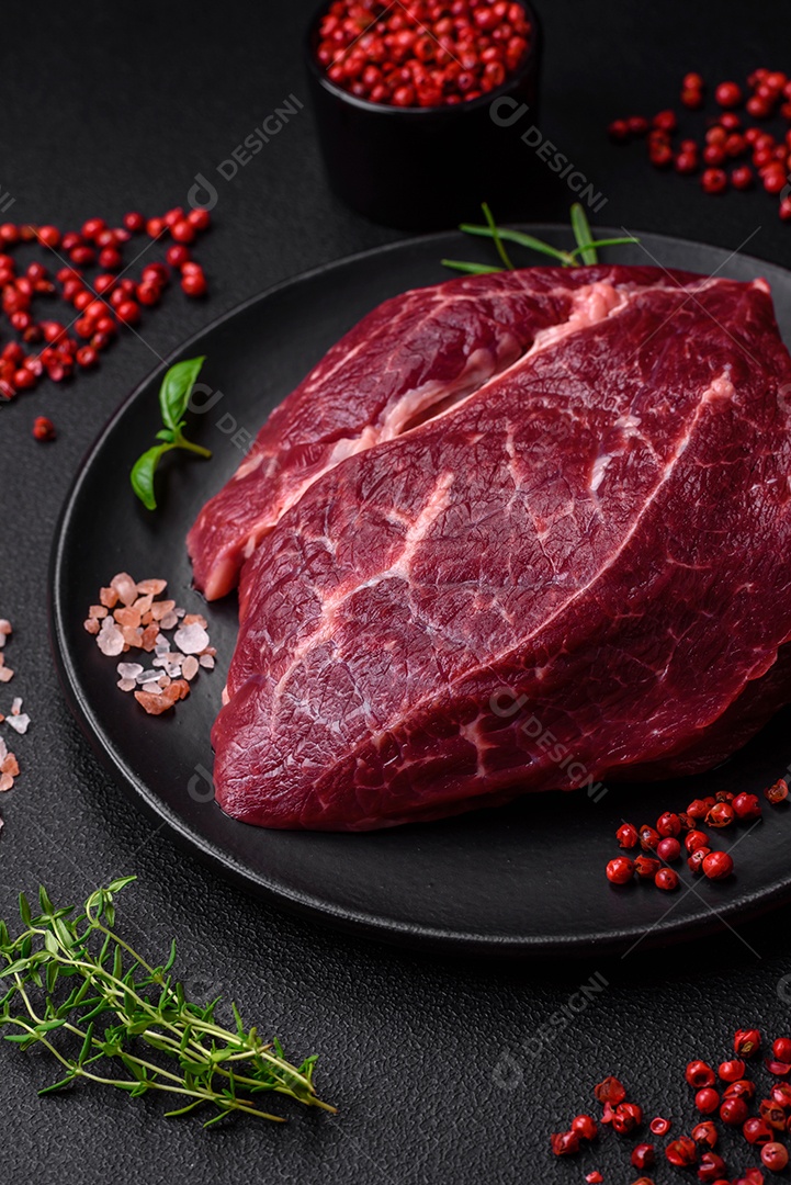 Carne crua suculenta com especiarias, sal e ervas sobre um fundo escuro de concreto. Preparando-se para cozinhar um prato de carne