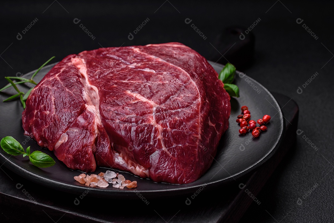 Carne crua suculenta com especiarias, sal e ervas sobre um fundo escuro de concreto. Preparando-se para cozinhar um prato de carne