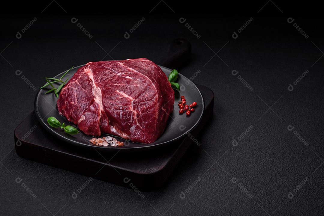 Carne crua suculenta com especiarias, sal e ervas sobre um fundo escuro de concreto. Preparando-se para cozinhar um prato de carne