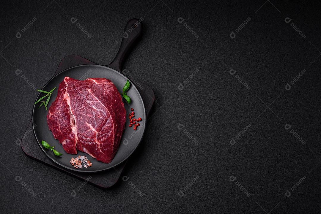 Carne crua suculenta com especiarias, sal e ervas sobre um fundo escuro de concreto. Preparando-se para cozinhar um prato de carne