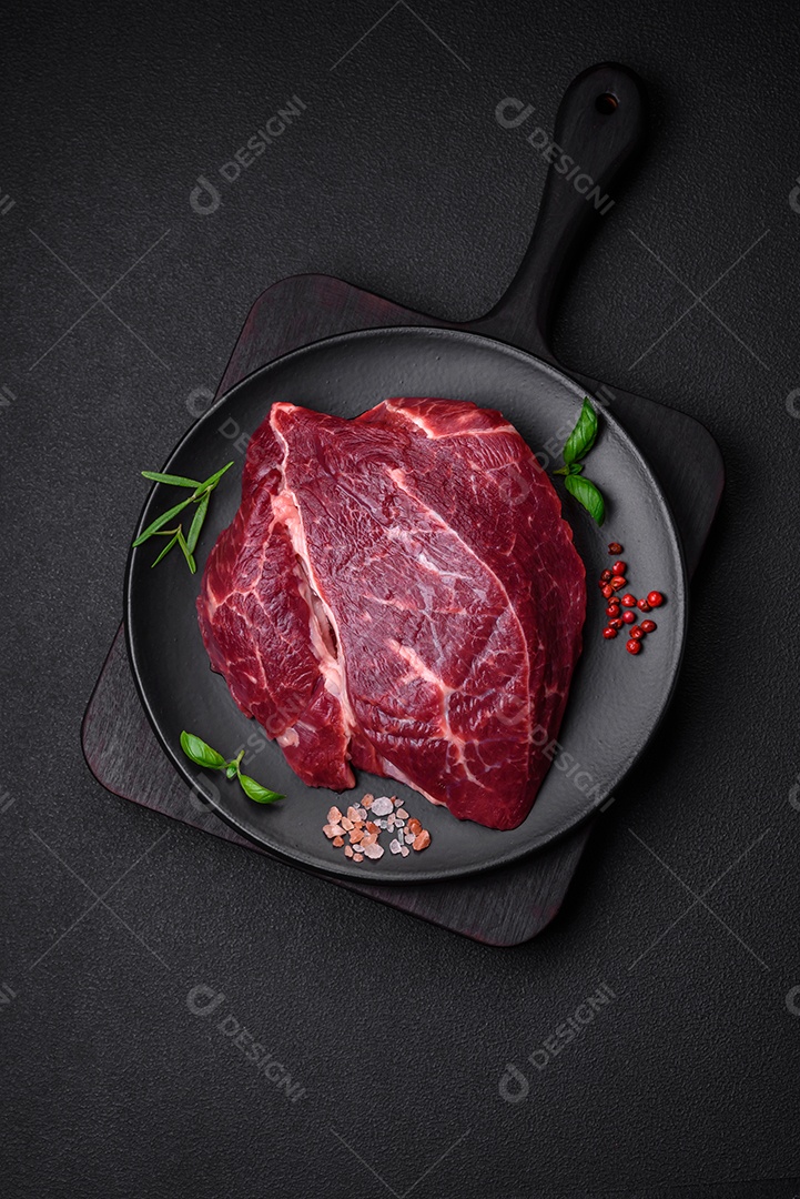 Carne crua suculenta com especiarias, sal e ervas sobre um fundo escuro de concreto. Preparando-se para cozinhar um prato de carne