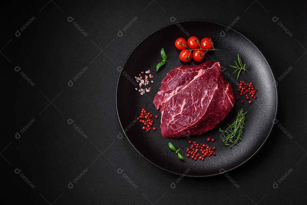 Carne crua suculenta com especiarias, sal e ervas sobre um fundo escuro de concreto. Preparando-se para cozinhar um prato de carne