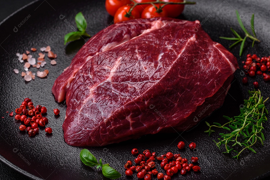 Carne crua suculenta com especiarias, sal e ervas sobre um fundo escuro de concreto. Preparando-se para cozinhar um prato de carne