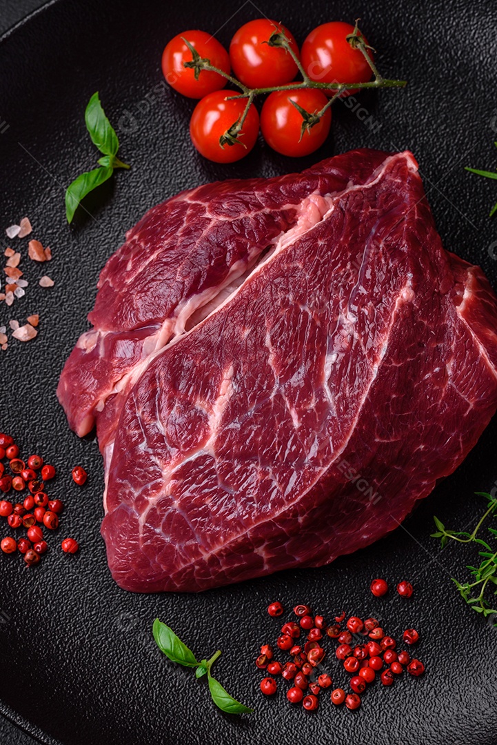 Carne crua suculenta com especiarias, sal e ervas sobre um fundo escuro de concreto. Preparando-se para cozinhar um prato de carne