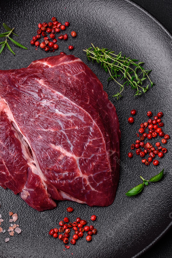 Carne crua suculenta com especiarias, sal e ervas sobre um fundo escuro de concreto. Preparando-se para cozinhar um prato de carne