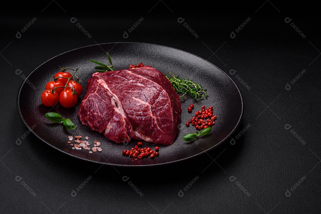 Carne crua suculenta com especiarias, sal e ervas sobre um fundo escuro de concreto. Preparando-se para cozinhar um prato de carne