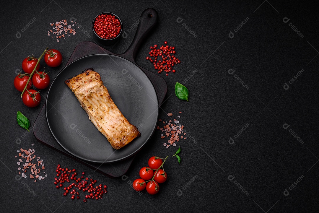 Fatia de delicioso peixe assado com sal, especiarias e ervas em uma placa cerâmica sobre um fundo escuro de concreto