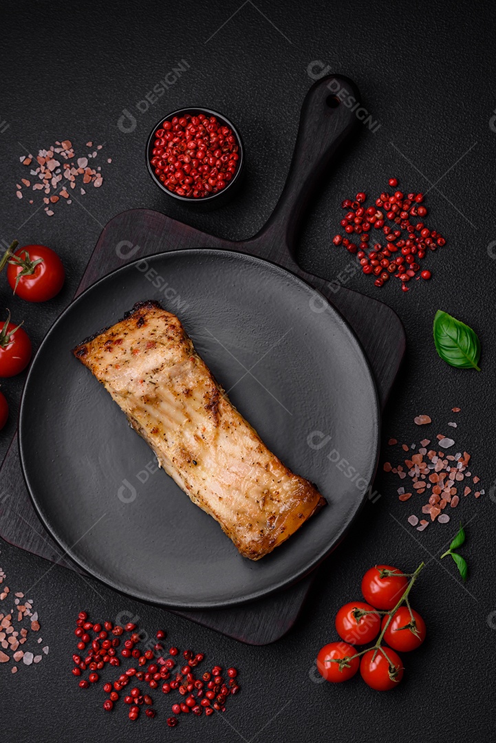 Fatia de delicioso peixe assado com sal, especiarias e ervas em uma placa cerâmica sobre um fundo escuro de concreto