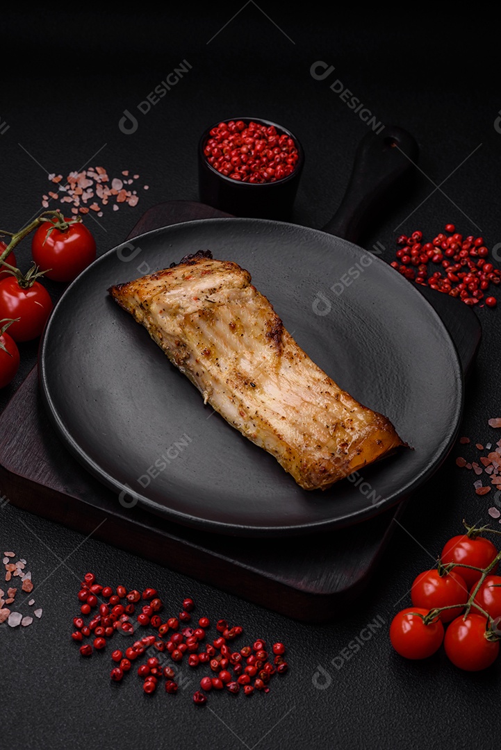 Fatia de delicioso peixe assado com sal, especiarias e ervas em uma placa cerâmica sobre um fundo escuro de concreto