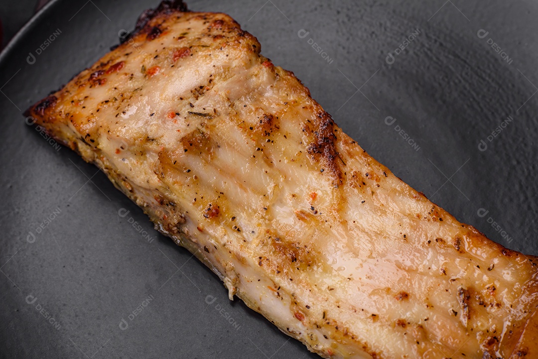 Fatia de delicioso peixe assado com sal, especiarias e ervas em uma placa cerâmica sobre um fundo escuro de concreto