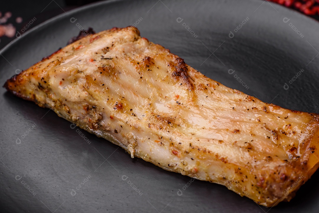 Fatia de delicioso peixe assado com sal, especiarias e ervas em uma placa cerâmica sobre um fundo escuro de concreto