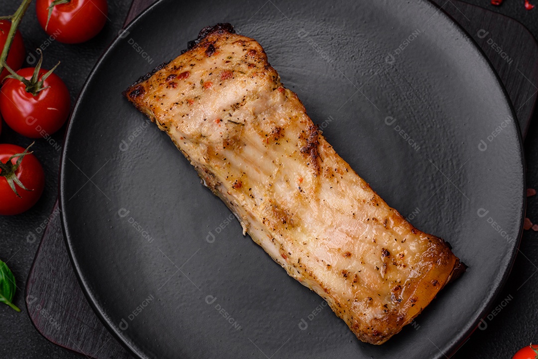Fatia de delicioso peixe assado com sal, especiarias e ervas em uma placa cerâmica sobre um fundo escuro de concreto