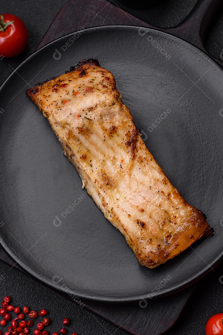 Fatia de delicioso peixe assado com sal, especiarias e ervas em uma placa cerâmica sobre um fundo escuro de concreto