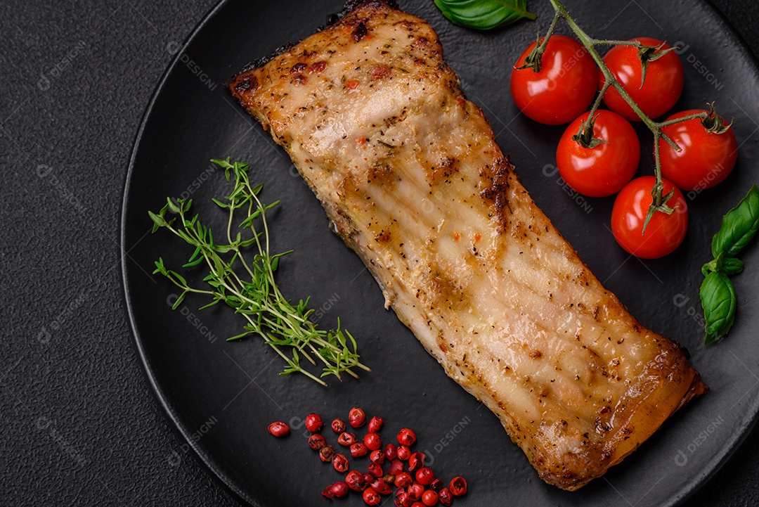 Fatia de delicioso peixe assado com sal, especiarias e ervas em uma placa cerâmica sobre um fundo escuro de concreto