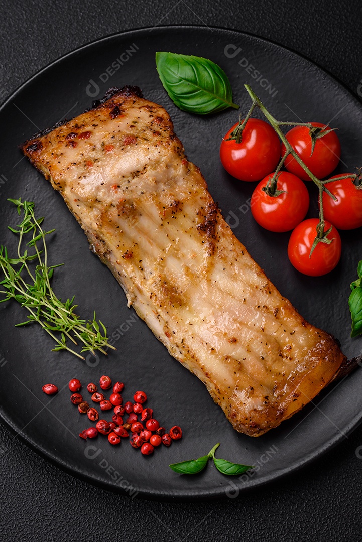 Fatia de delicioso peixe assado com sal, especiarias e ervas em uma placa cerâmica sobre um fundo escuro de concreto