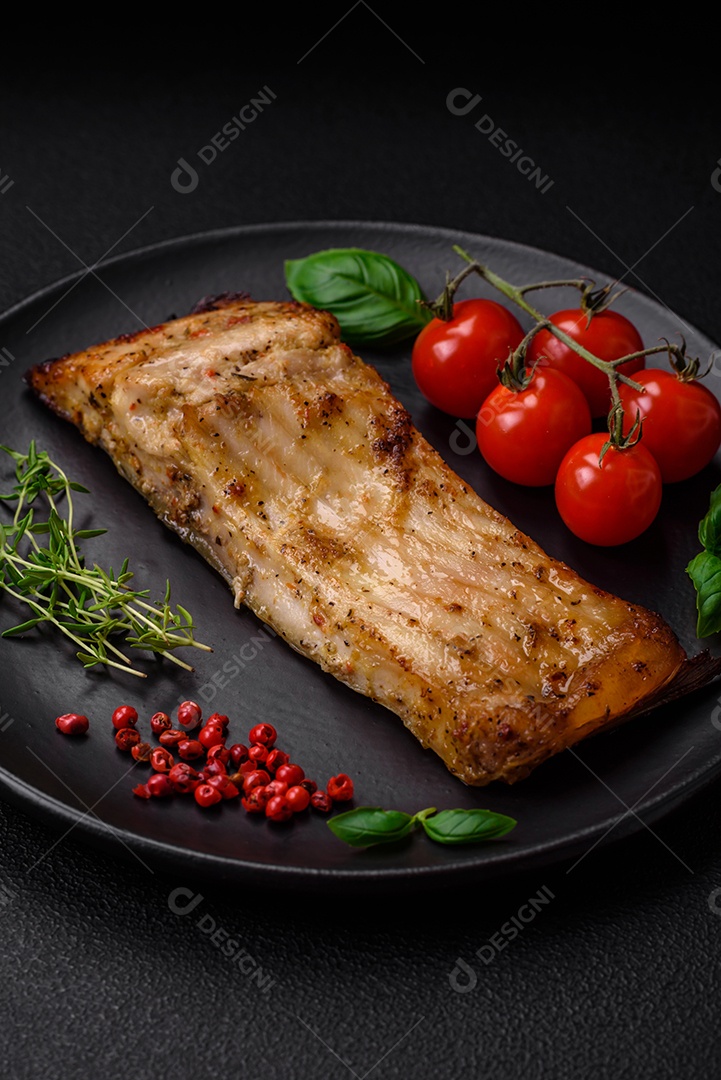 Fatia de delicioso peixe assado com sal, especiarias e ervas em uma placa cerâmica sobre um fundo escuro de concreto
