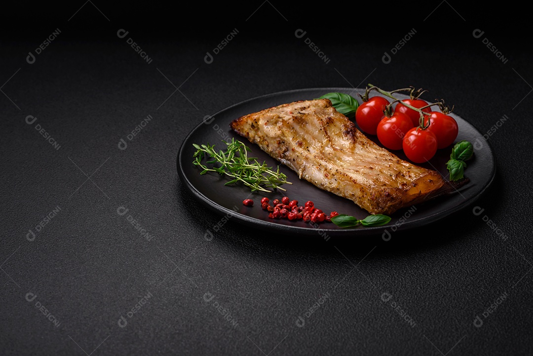 Fatia de delicioso peixe assado com sal, especiarias e ervas em uma placa cerâmica sobre um fundo escuro de concreto