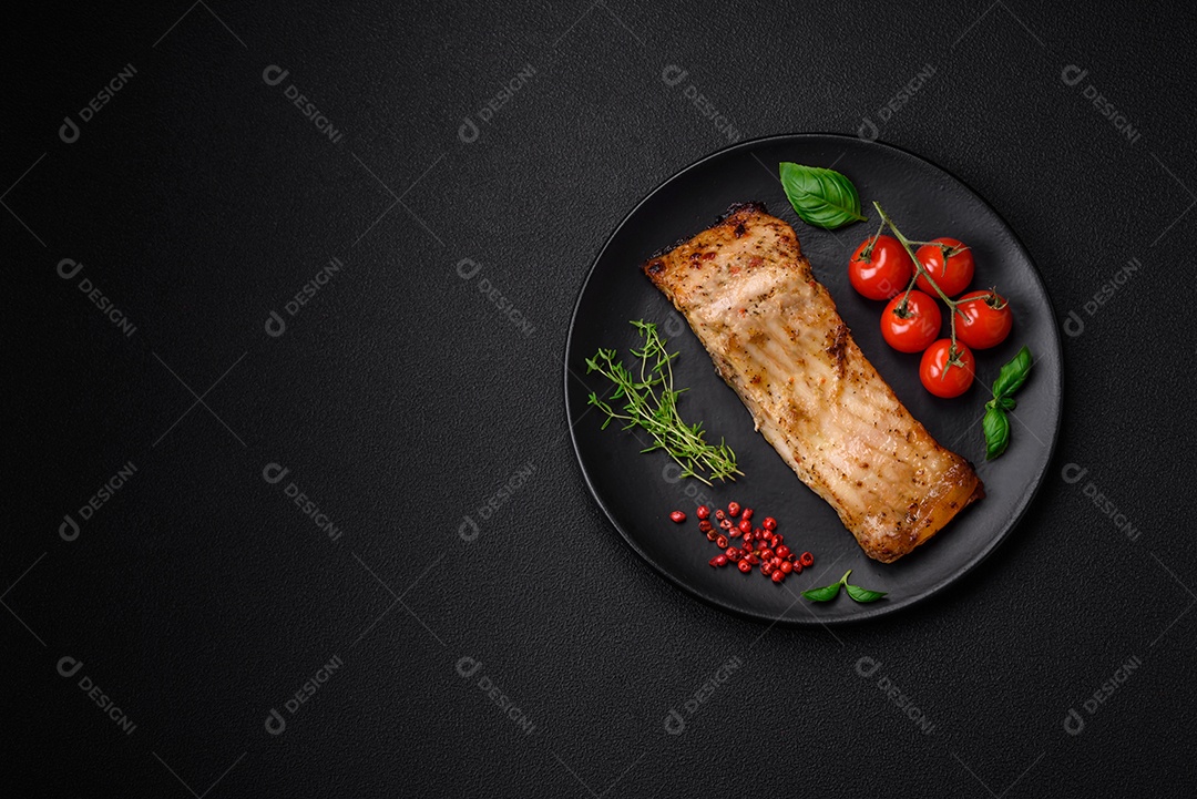 Fatia de delicioso peixe assado com sal, especiarias e ervas em uma placa cerâmica sobre um fundo escuro de concreto