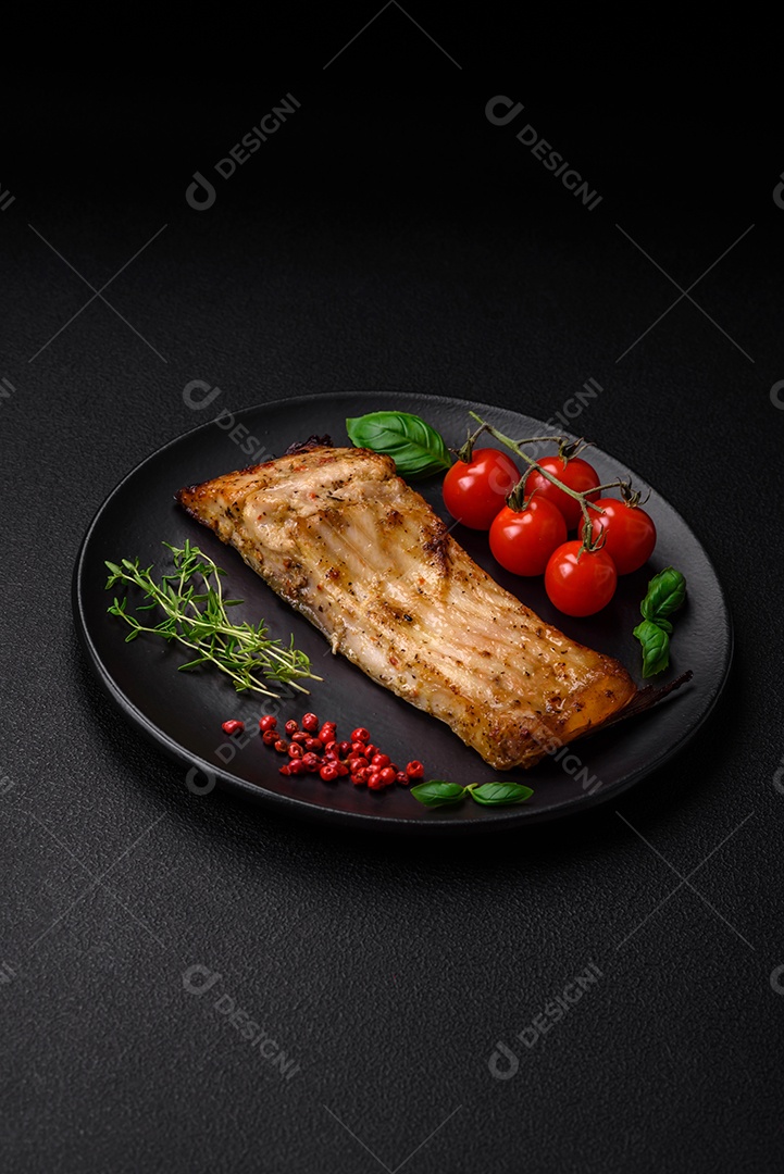 Fatia de delicioso peixe assado com sal, especiarias e ervas em uma placa cerâmica sobre um fundo escuro de concreto